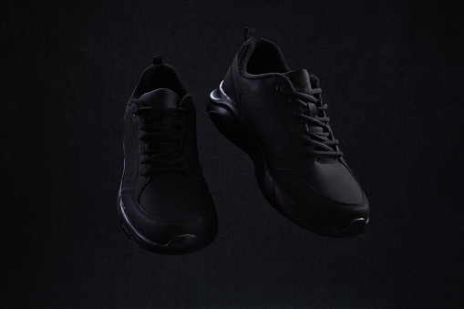 Pair of fashion black unbranded sneakers flying on dark background. Black running shoes levitate in air.