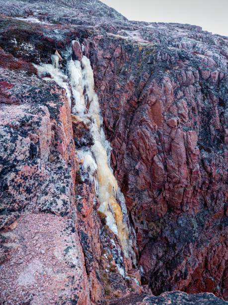 Frozen waterfall from a cliff. Atmospheric minimalist Arctic landscape with a hanging glacier on a rocky mountain top.
