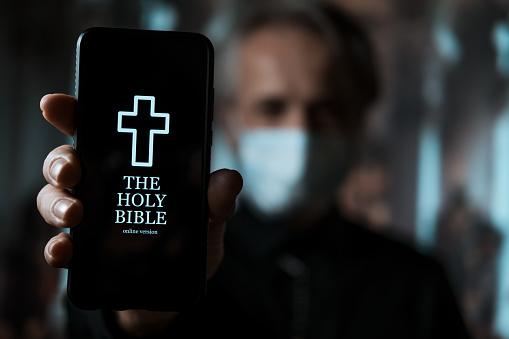 Priest holding smartphone with mobile version of Holy Bible