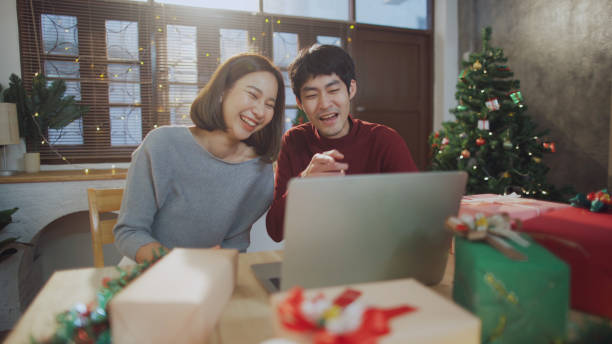 istock Happy Asian couple with video call while using laptop and opening Christmas gift box 1296145763