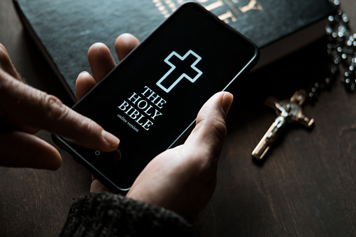 Man holding smartphone with mobile version of Holy Bible
