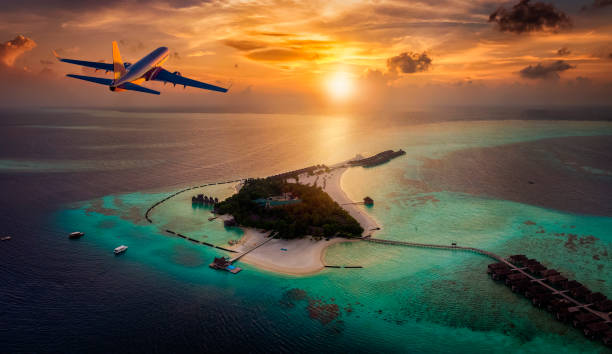 An airplane is approaching a tropical paradise island in the Maldives An airplane is approaching a tropical paradise island in the Maldives with turquoise during a colorful sunset planes flying overhead stock pictures, royalty-free photos & images