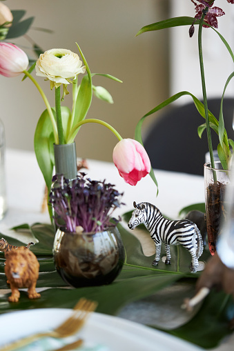 a close up of a jungle-themed table setting with a toy zebra and lion among the flower decorations, high resolution photo with copy space