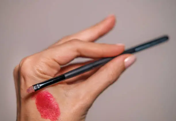Photo of Hand holding a Make-up brush. Lipstick on skin