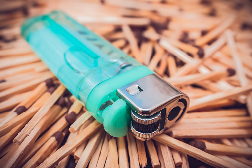 A new pocket lighter filled with gas lies on old, wooden matches