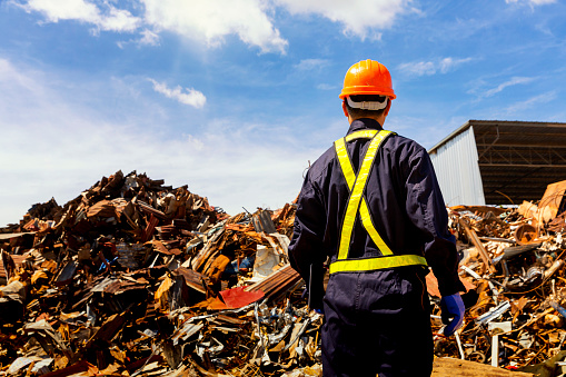 An engineer watching the steel to be brought into a recycling plant. Engineer and Recyclable material. Foreman wearing protective equipments and holding tablet and looking at Recyclable material.