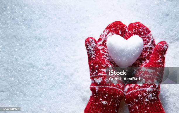 Female Hands In Knitted Mittens With Snowy Heart Against Snow Background Stock Photo - Download Image Now