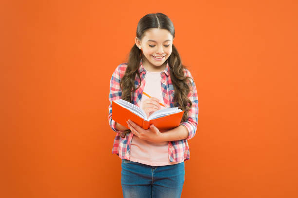 istock Study language. Making notes. Child doing homework writing in workbook. Girl hold book and pen. Girl cute write down idea notes. Notes to remember. Write essay or notes. Exercising writing workbook 1296161126