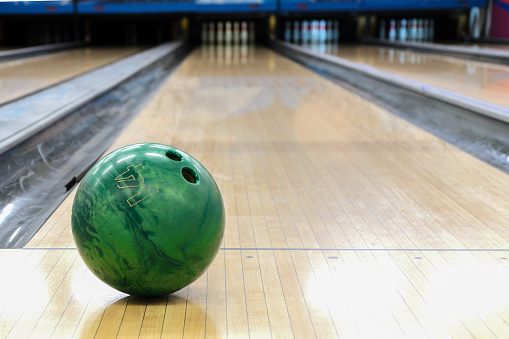 Close-up of green bowling ball against background of empty lanes in bowling alley. Active leisure. Sports activities for whole family. Space for text.