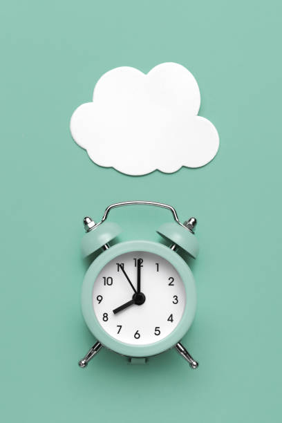 istock Classic round alarm clock and white clouds on the mint green background. 1296163664