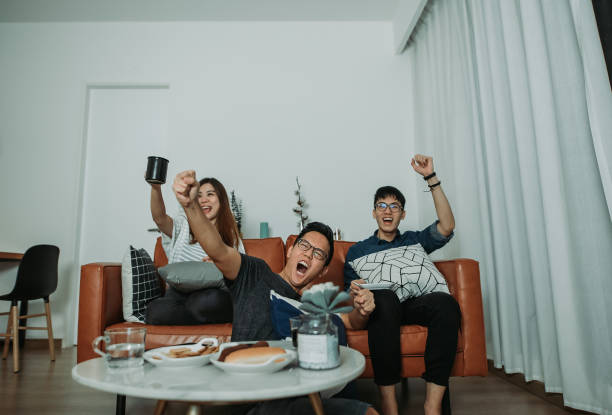 amigos chineses asiáticos assistindo a um jogo esportivo na televisão juntos em sua casa - family sofa night indoors - fotografias e filmes do acervo