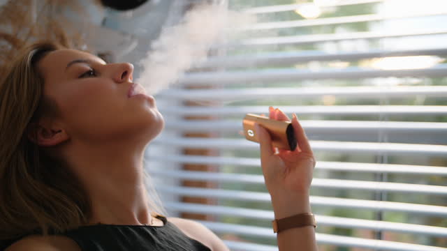 Woman Enjoying Electronic Cigarette. Vaping in living room