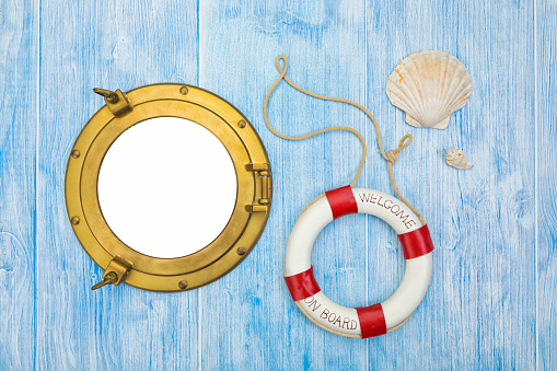 Maritime background, lifebuoy and sea shells on blue painted wood, brass porthole with copy space