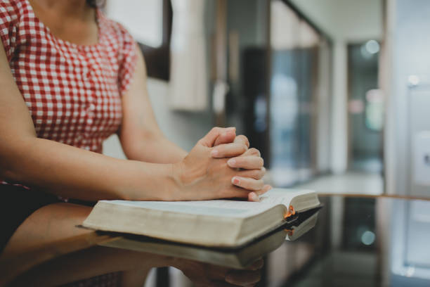 istock woman's hands praying on open bible while sitting on the sofa at home 1296169346