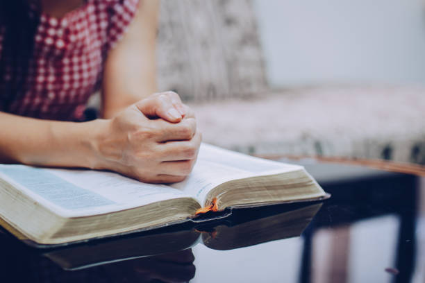 istock woman's hands praying on open bible while sitting on the sofa at home 1296169347