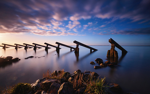 Icebreakers on the shore of Marken during sunrise. The sky is filled with clouds that are slightly grey/pink/purple colored. The water reflects the icebreakers and the different colors of the sky.