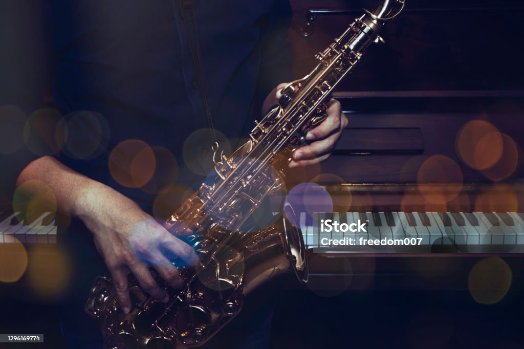 a musician plays alto saxophone over the piano a musician plays alto saxophone over the piano with Bokeh light  background Jazz Music Stock Photo