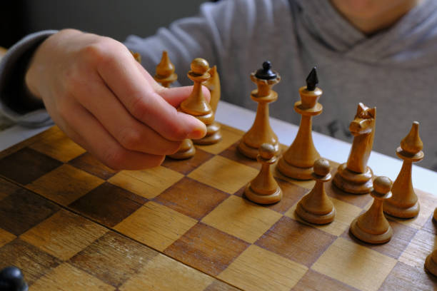 istock hand with white pawn across chess board close-up. Playing chess. Strategy, planning concept 1296170406