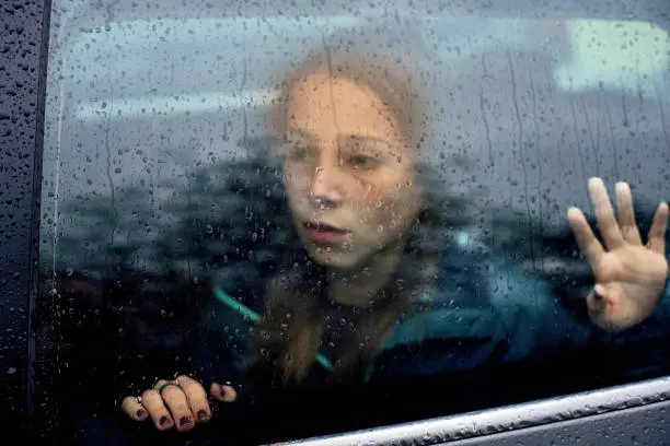 Sullen Sad woman looking through a steamy car window