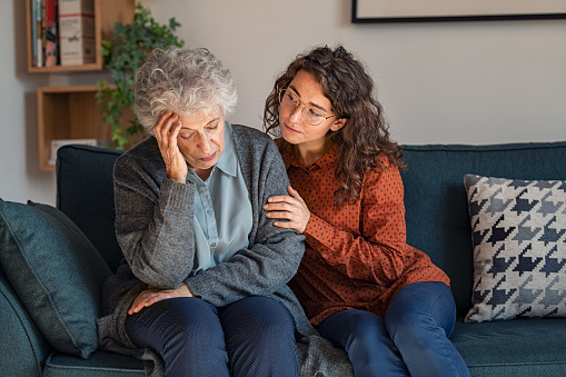 Caring daughter comforting frustrated unhappy senior woman. Loving adult granddaughter talking to sad depressed old grandmother holding hand and comforting her. Upset widowed woman with headache consoled by her daughter.