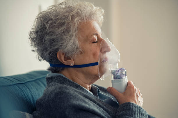Sick senior woman making inhalation with nebulizer Portrait of a ill senior woman making inhalation at home. Close up of an elderly woman holding mask nebulizer inhaling fumes medication into lungs with closed eyes. Self treatment of the respiratory tract using inhalation nebulizer. medical oxygen stock pictures, royalty-free photos & images