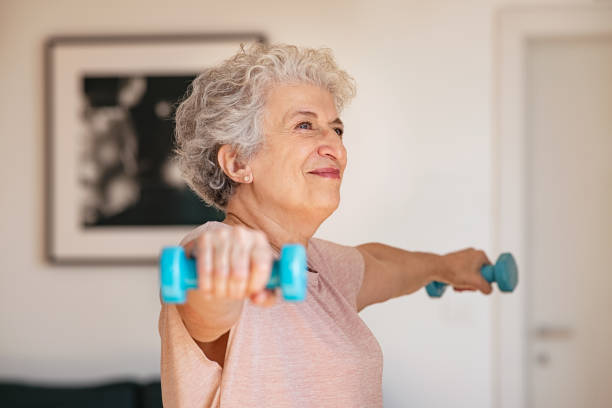 Senior woman exercising with dumbbells at home Senior woman lifting weights and working out at home. Old woman doing arms stretching exercise using weight dumbbells. Retired lady exercising with light weights. home workout stock pictures, royalty-free photos & images