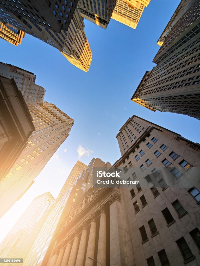 Buildings of Wall Street towering overhead against a blue sky background in the historic financial district of New York City Buildings of Wall Street towering overhead against a blue sky background in the historic financial district of lower Manhattan in New York City New York Stock Exchange Stock Photo