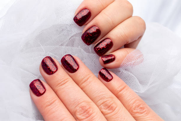 istock Female hands with beautiful manicure - dark red glittered nails in white tulle fabric. Selective focus 1296183629