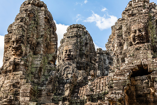 The Bayon Temple is a richly decorated Khmer temple at Angkor in Cambodia. Built in the late 12th or early 13th century as the state temple of the Mahayana Hindu King Jayavarman VII, the Bayon stands at the centre of Jayavarman's capital, Angkor Thom. Following Jayavarman's death, it was modified and augmented by later Theravada Buddhist kings in accordance with their own religious preferences.\nThe Bayon's most distinctive feature is the multitude of serene and smiling stone faces on the many towers which jut out from the upper terrace and cluster around its central peak