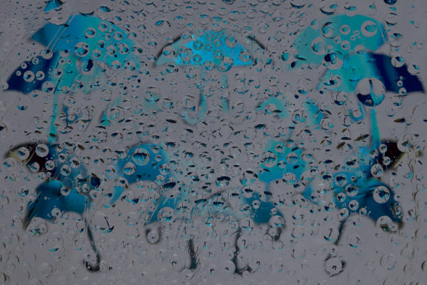 istock Rain. Raindrops fall down against the gray background with blue umbrella silhouettes and their reflections. 1296184930
