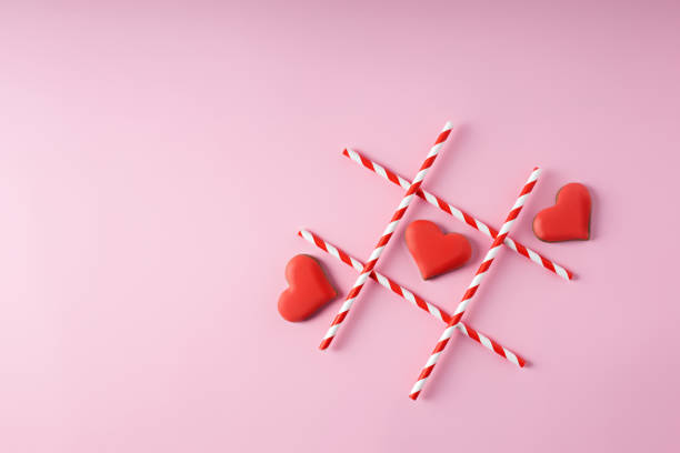 istock Tic-tac-toe with straws and red hearts on pink background 1296191682