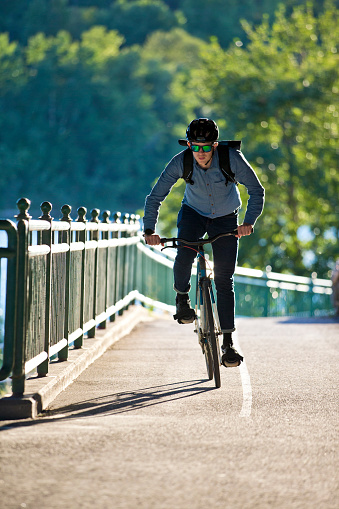 A male bicycle commuter in a large city rides a designated bicycle lane on his way home from work. He rides a one-speed or fixed-gear bicycle with just a front brake. He wears casual clothing, a cycling helmet and, carries a bike messenger style backpack.