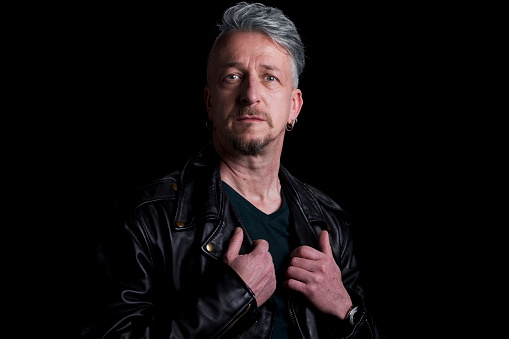 Portrait of serious mature man standing against black background.