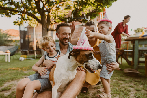 Photo of a young family with two kids being all cheerful and playful because they are celebrating their dog's birthday in the backyard