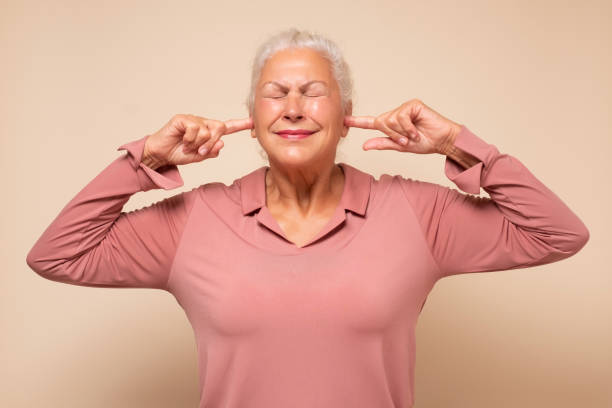 istock Angry annoyed senior woman plugging her ears to avoid loud noise 1296196850