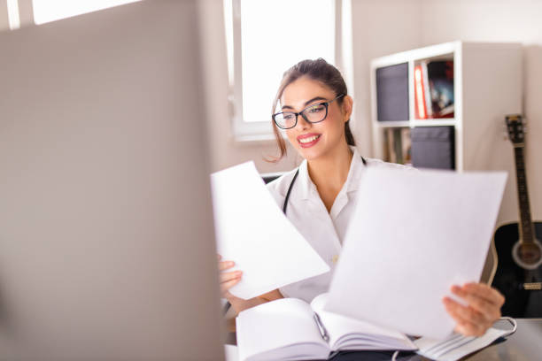 istock Young female doctor checking medical document and using computer at her office 1296198500