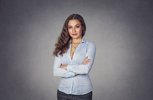 Portrait of young attractive brunette woman with crossed arms, folded hands isolated on gray background