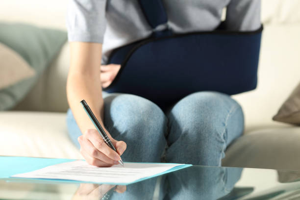 Handicapped woman with sling signing contract Front view of a handicapped woman with sling signing contract at home claim form photos stock pictures, royalty-free photos & images