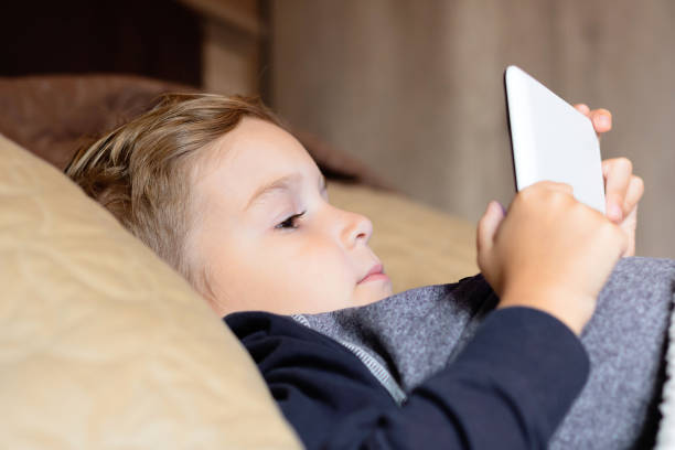 istock Little boy lying down on bed and surfing the net on touchpad. 1296211929
