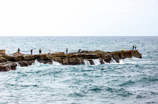 Wollongong, Australia - December 30, 2020: Group of fishermen catching fish on rocky coastline near Wollongong NSW, background with copy space, full frame horizontal composition