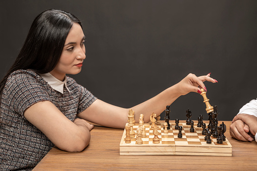 Woman portrait of elegant suit playing on fine wooden chess board.
