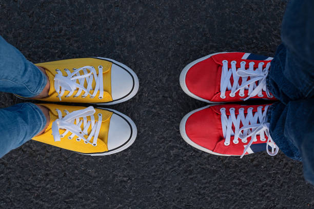 Man and woman of red and yellow sneakers stand opposite each other on a asphalt background, the top view. Man and woman of red and yellow sneakers stand opposite each other on a asphalt background, the top view. pair stock pictures, royalty-free photos & images