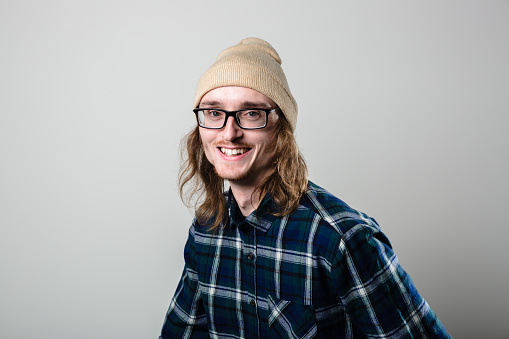 Studio portrait of a real man in his late 20s wearing glasses and a beanie and plaid shirt.