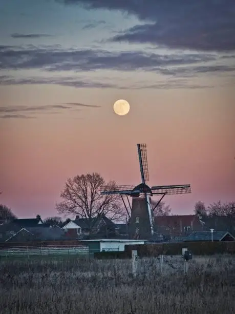 Photo of dutch windmill at winter sunset with full moon on the sky