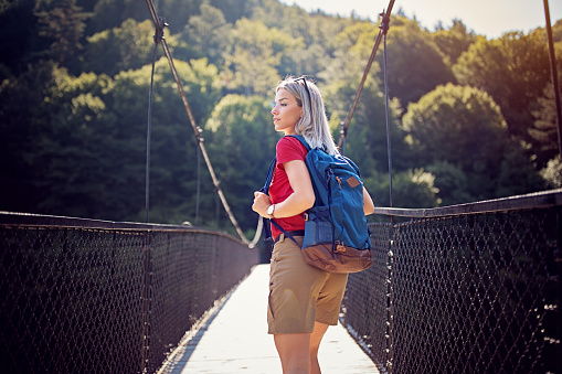 Hiker woman is walking a rope bridge over river in the forest
