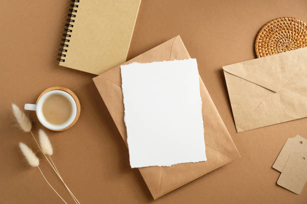 istock Blank paper card and envelope mockup on brown table with cup of coffee, notepad, dried flowers. Flat lay. Top view. 1296216890