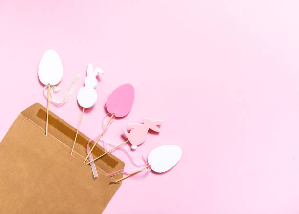 istock Easter composition with traditional decor. Decorative colorful egg and rabbit wooden figures in craft paper envelope on light pink paper background. 1296217890