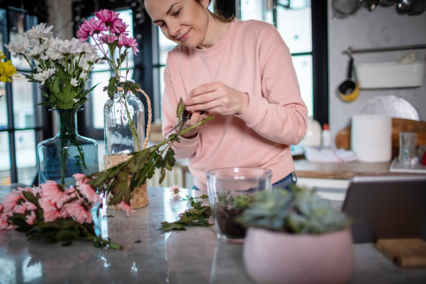 istock Young woman at the kitchen table arranging flowers in vase. 1296220237