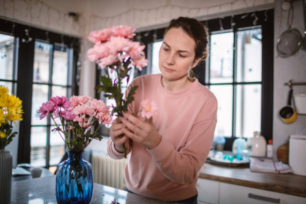istock Young woman at the kitchen table arranging flowers in vase. 1296220251