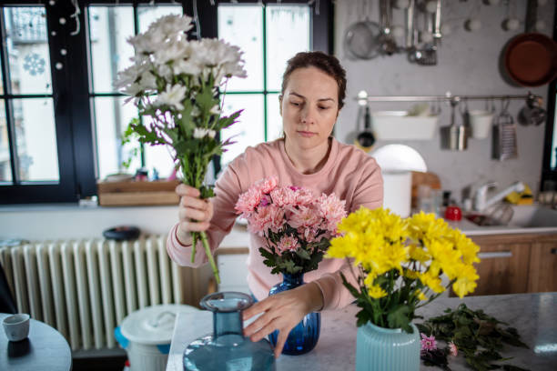 istock Young woman at the kitchen table arranging flowers in vase. 1296221132